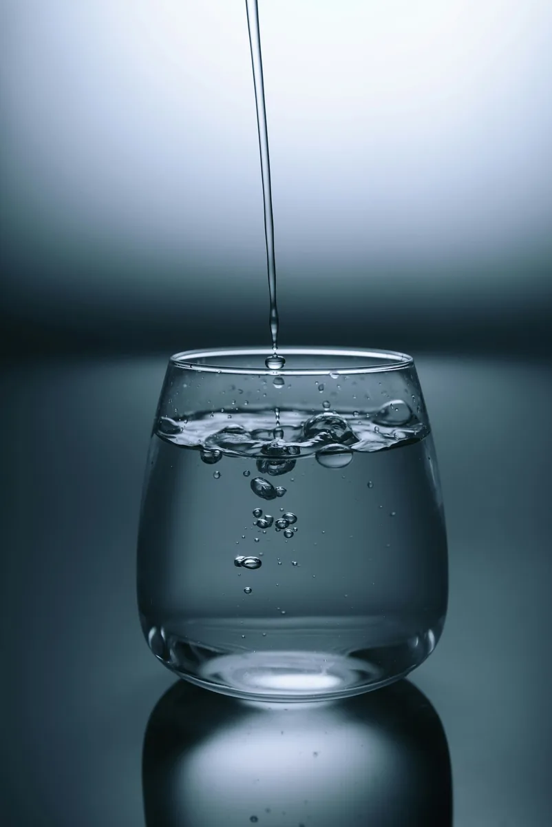 Vaso de agua fresca sobre una superficie clara, importancia de hidratarse